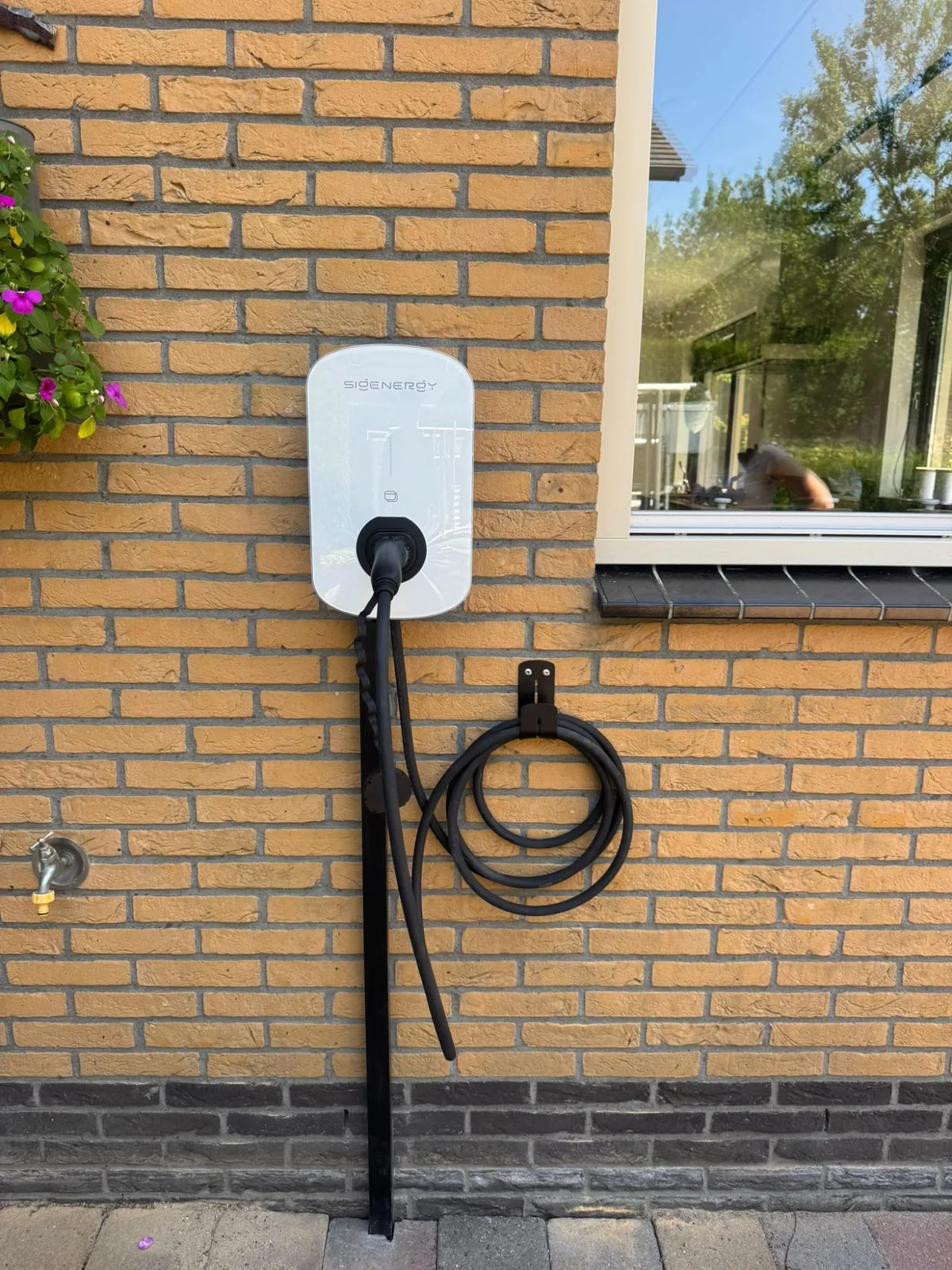 Sigenergy-laadpaal aan een bakstenen gevel met kabelhouder